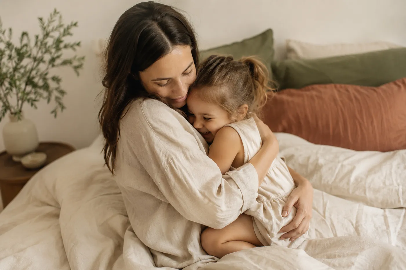 Mother and young child hugging on a bed with a cream comforter